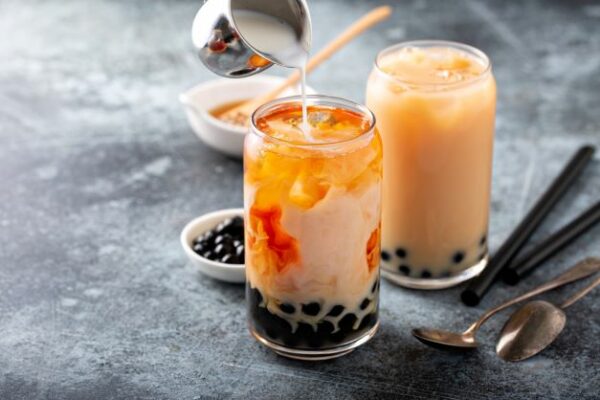 Two glasses being filled with Thai Tea and Milk with Boba